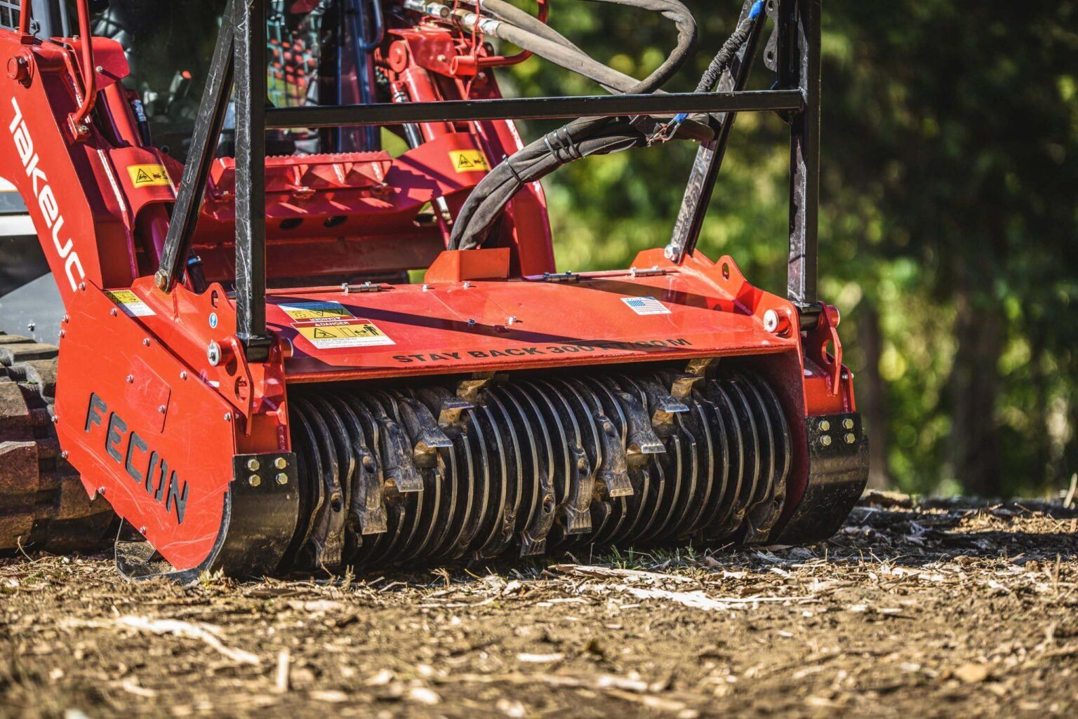 A compact track loader with a drum mulcher head working on chipped ground outdoors.